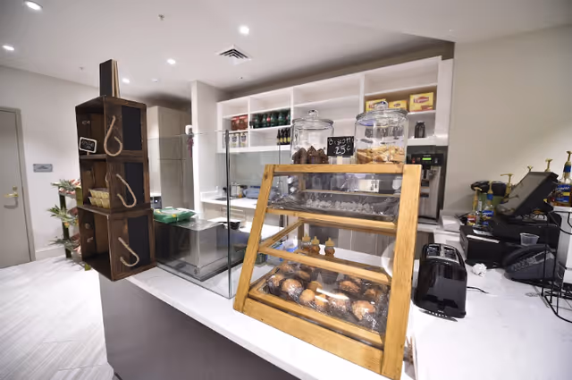 A modern indoor cafe counter with a glass pastry display case, jars of cookies, shelving, and a cash register.