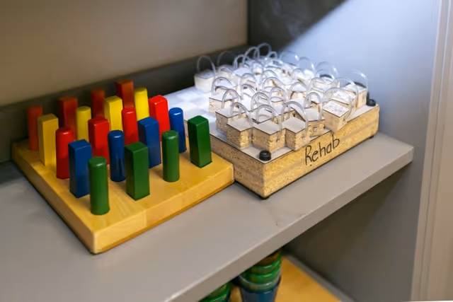 Wooden rehabilitation pegboard puzzles and therapy games on a gray shelf, one block set labeled "Rehab".