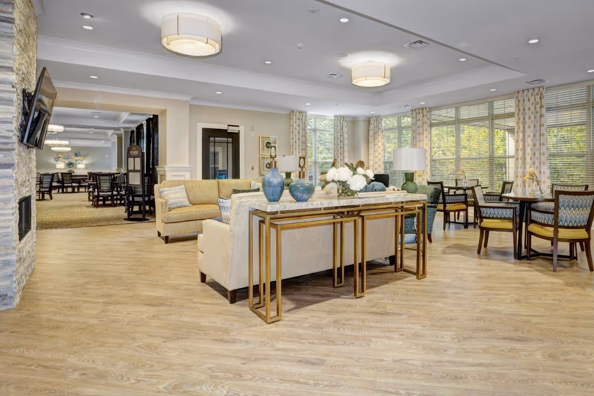 Spacious, well-lit communal living and dining area with sofas, tables, chairs, and large windows.