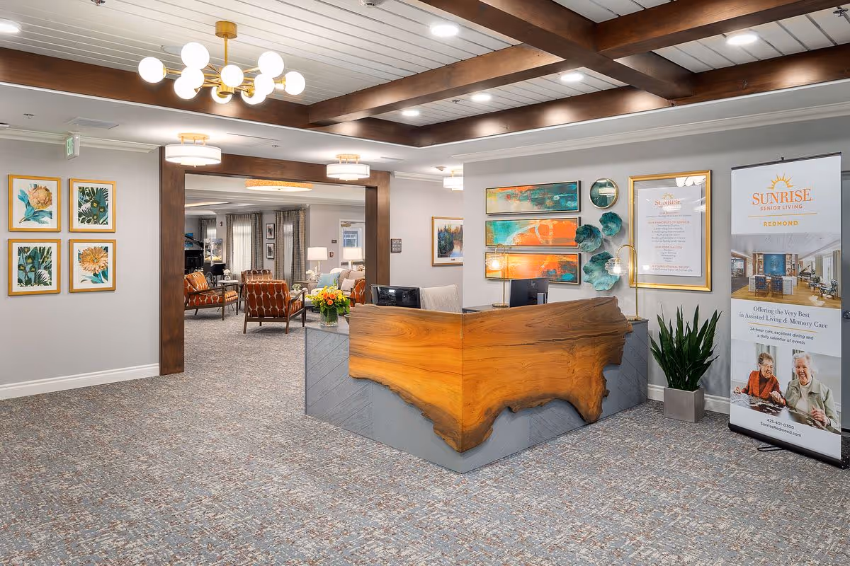 Reception lobby with a live-edge wood front desk, seating area, colorful wall art, and a Sunrise Senior Living banner.
