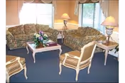 A cozy sitting area with floral-upholstered sofas and chairs around a white coffee table, table lamps, and bay windows with curtains.