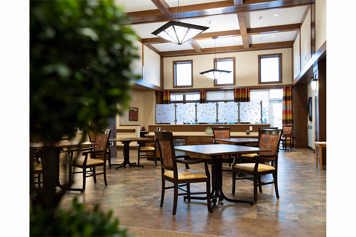 Spacious senior community dining room with several tables and chairs beneath coffered ceilings and pendant lights.