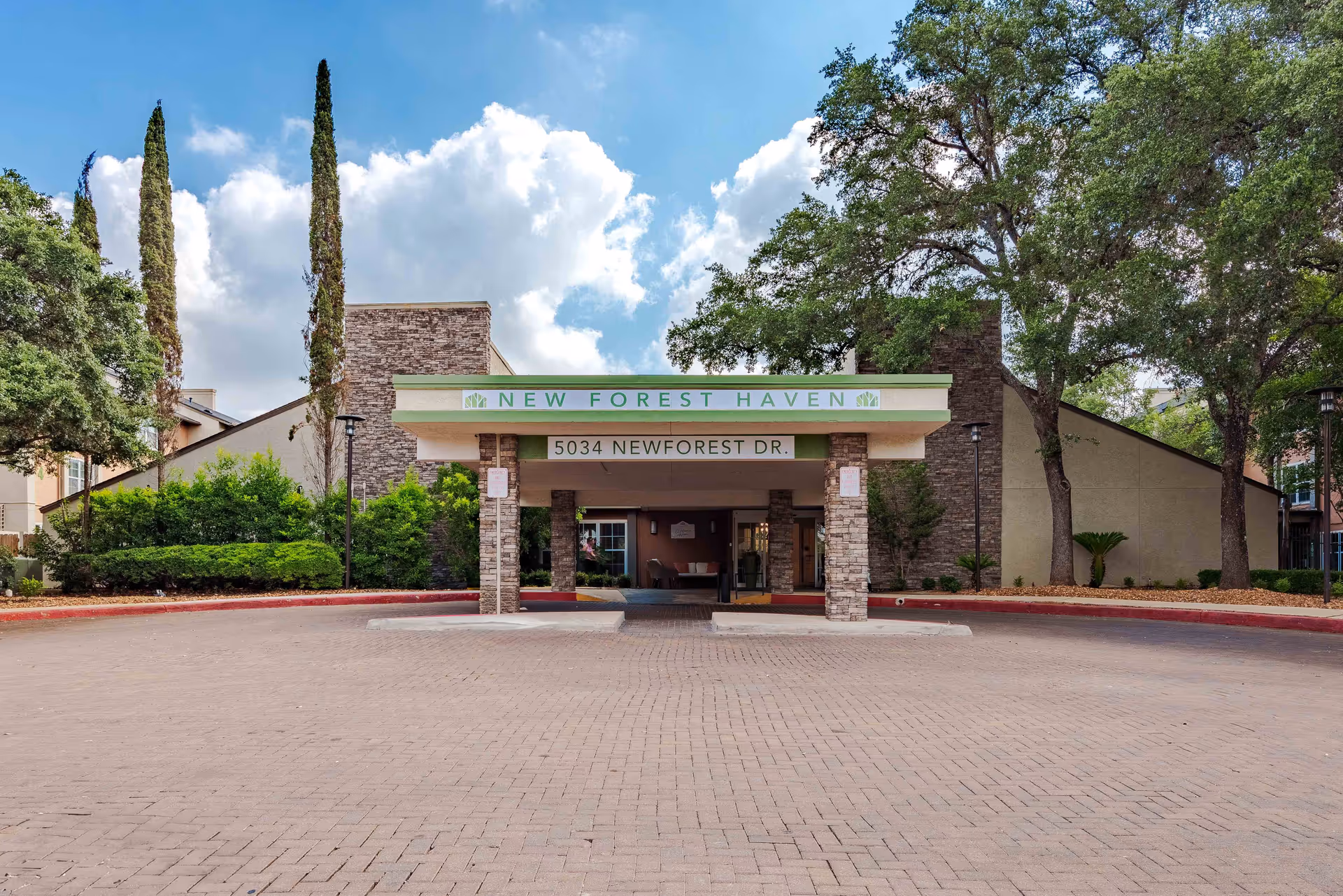 Front exterior view of New Forest Haven facility with a covered entrance, stone pillars, and surrounding trees and bushes under a partly cloudy sky.