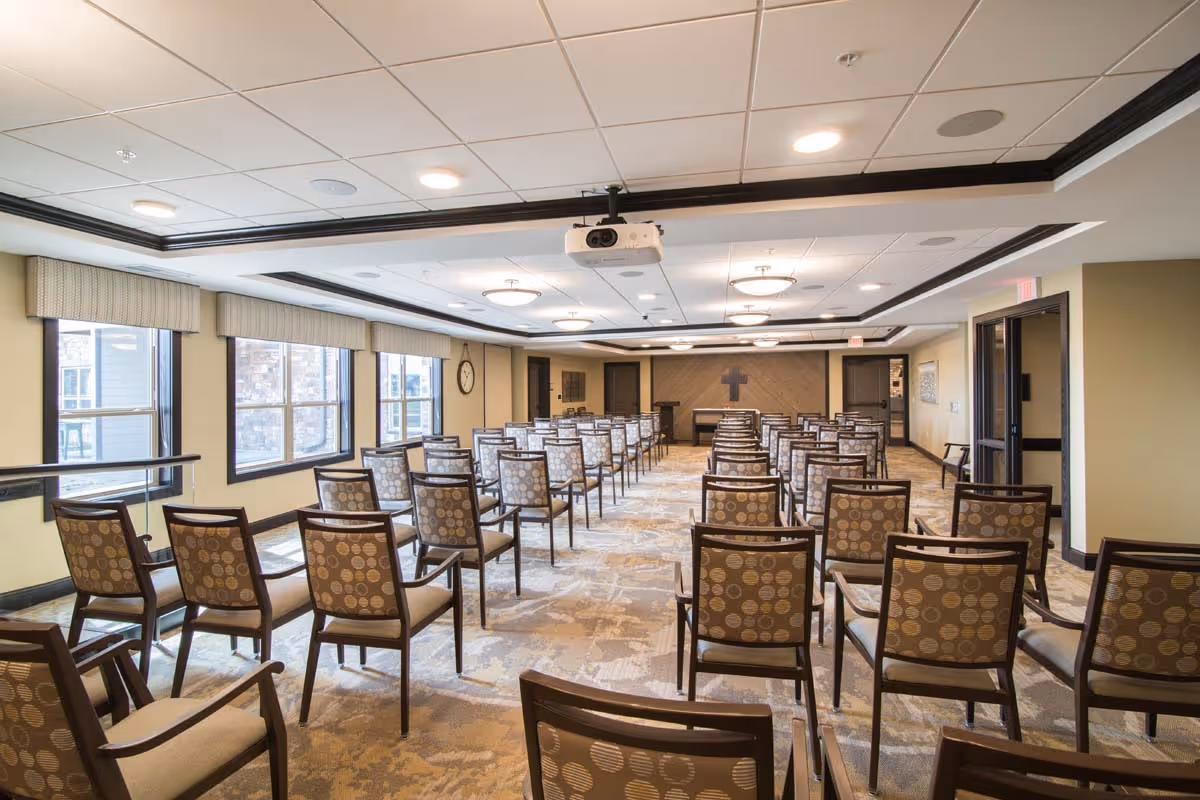 Spacious interior meeting room with rows of patterned chairs facing a lectern and projector at the front.