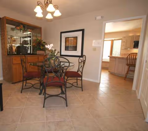 Dining room with glass table, wrought-iron chairs, sideboard, and framed wall art.
