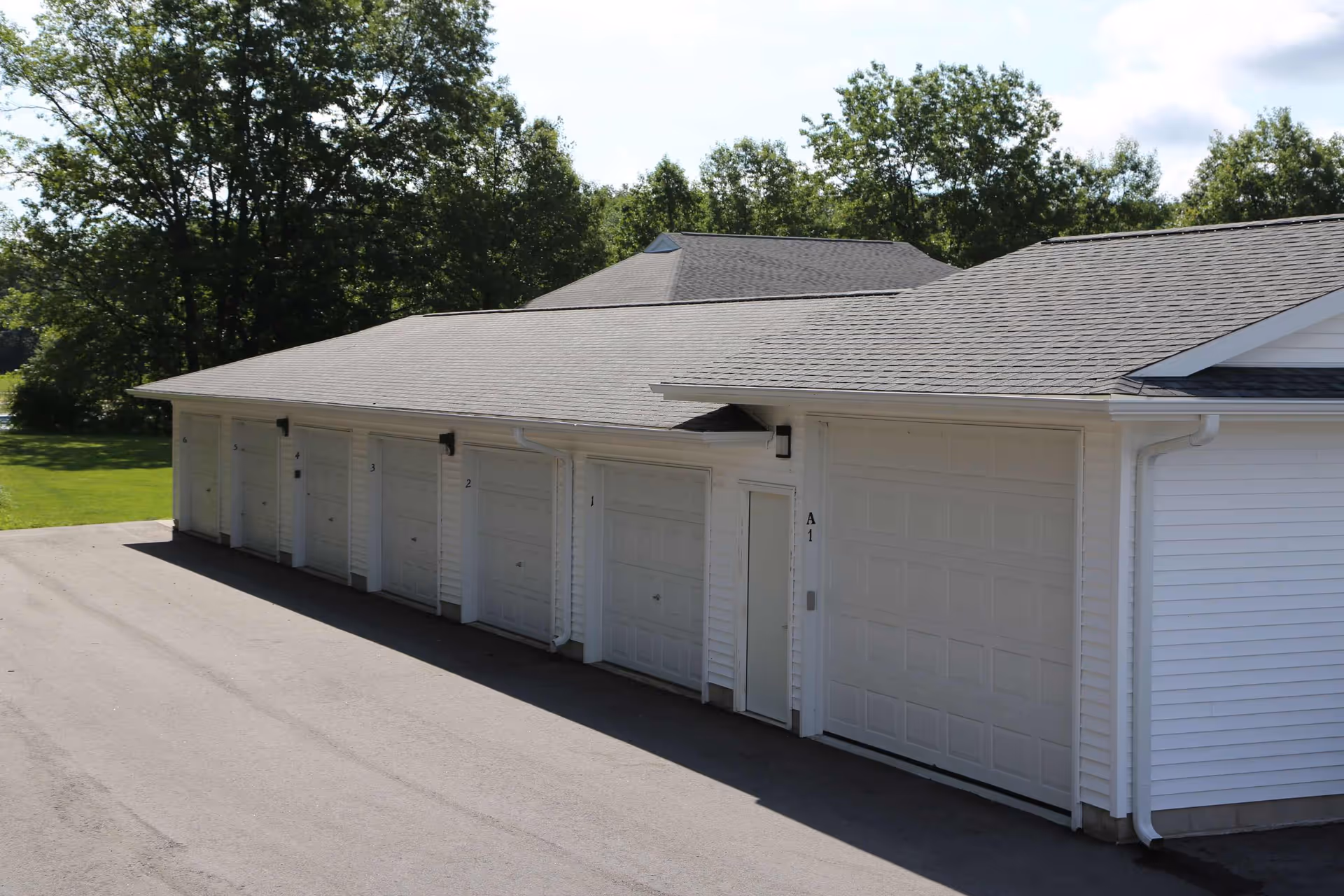 A row of attached white garage doors on a single-story building with trees and lawn in the background.