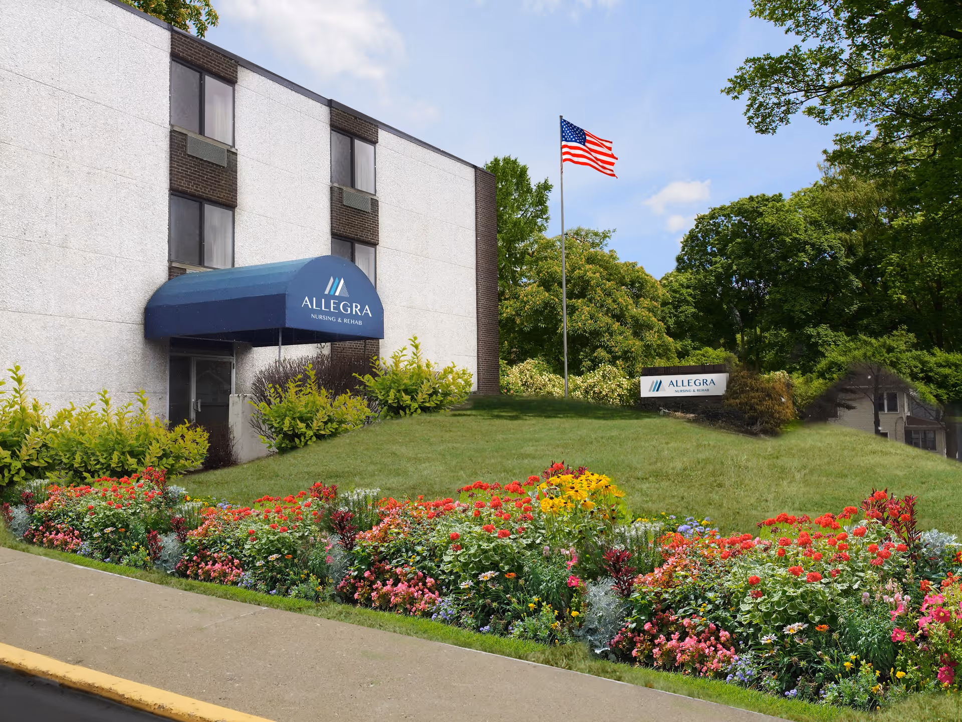 Exterior front of Allegra nursing and rehab building with a blue awning, an American flag, and colorful flower beds.