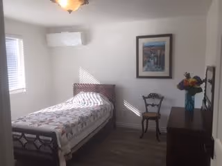 Small bedroom with a single bed, wooden dresser, two chairs, a framed picture, window, and wall-mounted air conditioner.