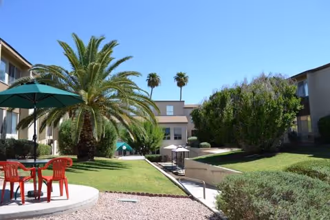 Copper Heights outdoor courtyard with palm trees, green lawn, and red chairs under umbrellas.