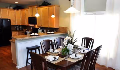 Wood dining table set for a meal with a floral centerpiece in a kitchen-adjacent dining area.
