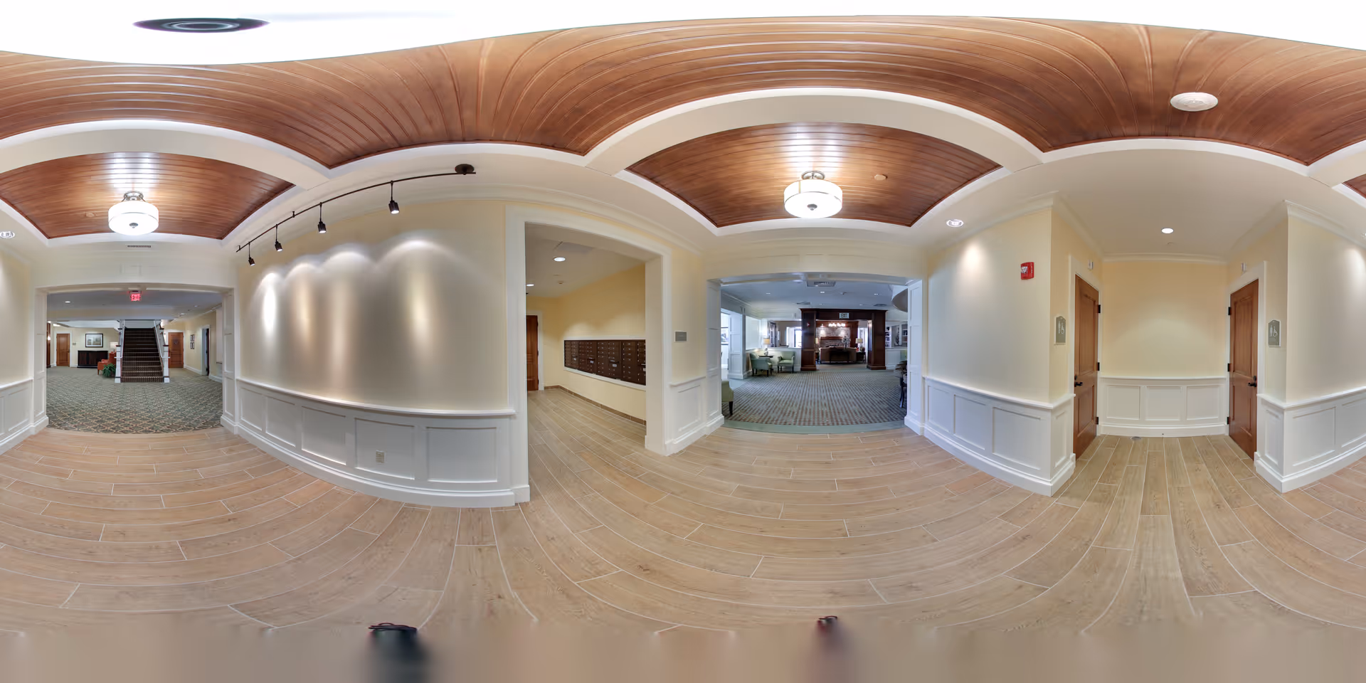 Spacious interior foyer with wood-paneled curved ceilings, recessed and pendant lighting, tile floor, white wainscoting, and openings into a carpeted lounge and mail area.