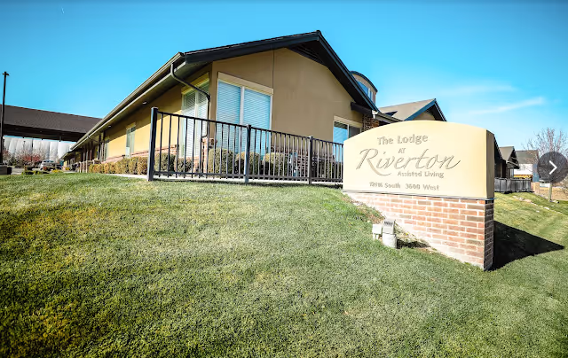 Exterior view of The Lodge at Riverton assisted living building with a sign on a grassy lawn.