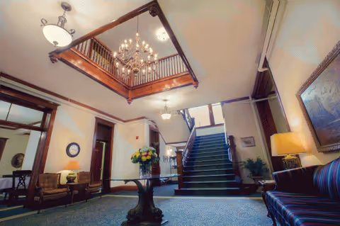 Rathbone Home lobby interior with grand staircase, chandelier, seating, and flowers.