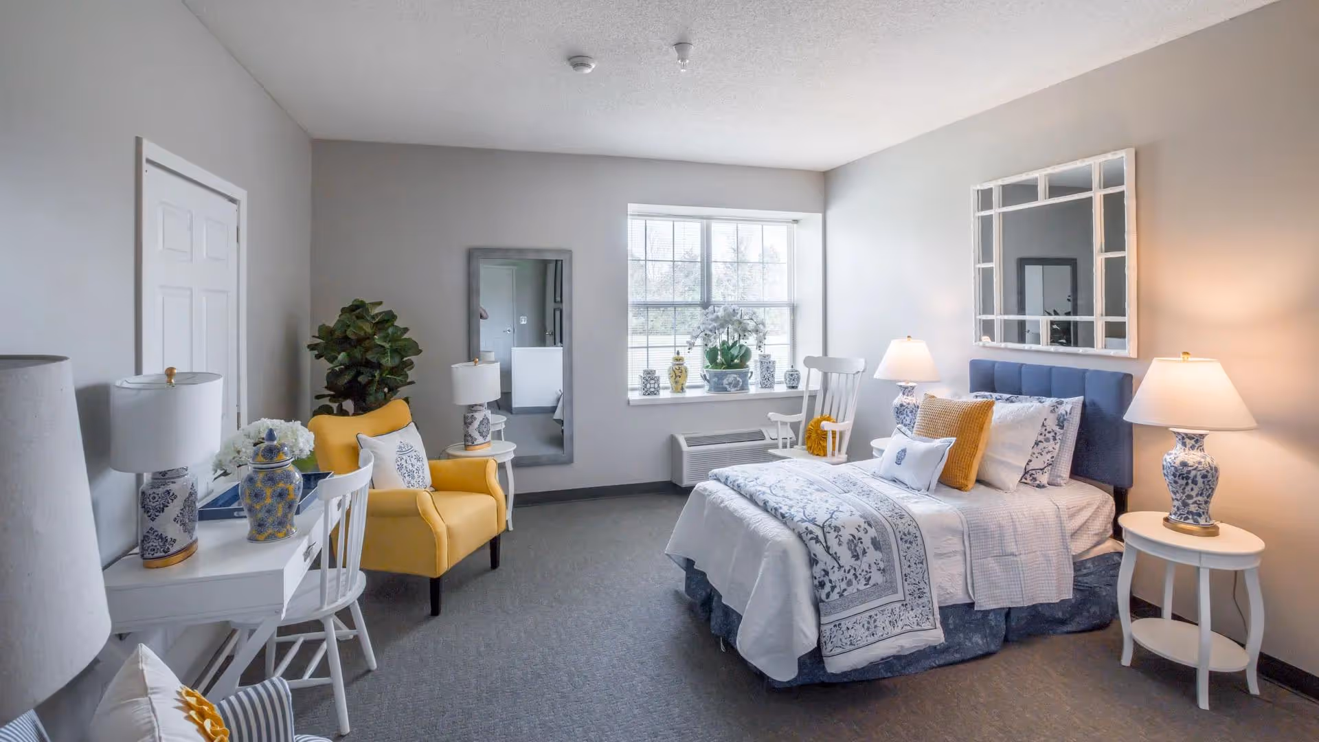 Bright furnished bedroom with a bed, bedside tables and lamps, a yellow armchair, desk and window.