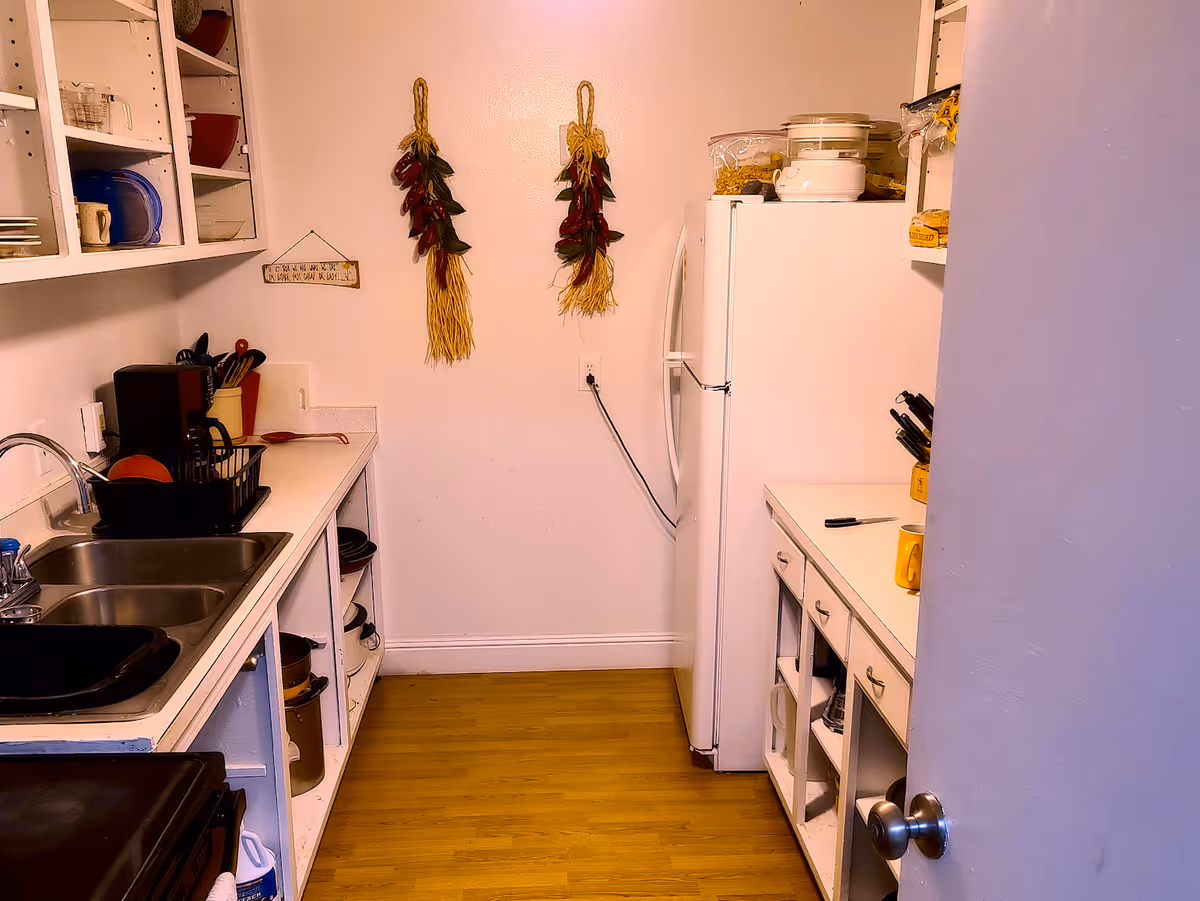 Small galley kitchen with a sink, open shelving, countertops, refrigerator, and decorative hanging peppers on the wall.