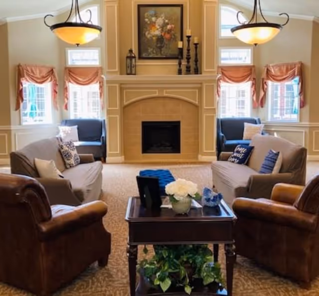 Cozy communal living room with sofas and armchairs arranged around a coffee table facing a central fireplace and decorative chandeliers.
