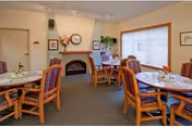 Dining room with round tables and cushioned chairs arranged near a fireplace and a window.