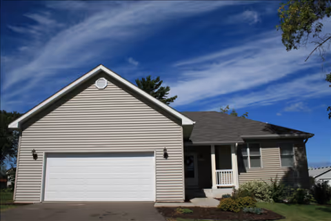 A beige, single-story building with a two-car garage and front porch.
