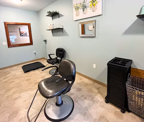 Small salon-style room with two styling chairs, wall-mounted shelves, a mirror, and storage against a pale blue wall.