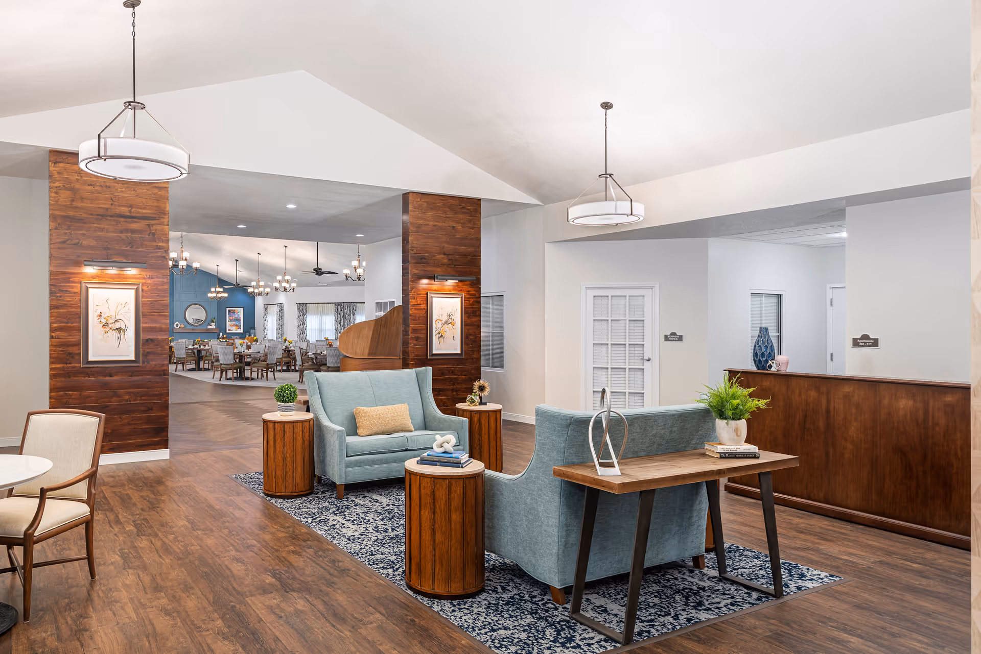 Spacious senior living facility lobby with teal seating, wooden accents, and a view into the dining area.