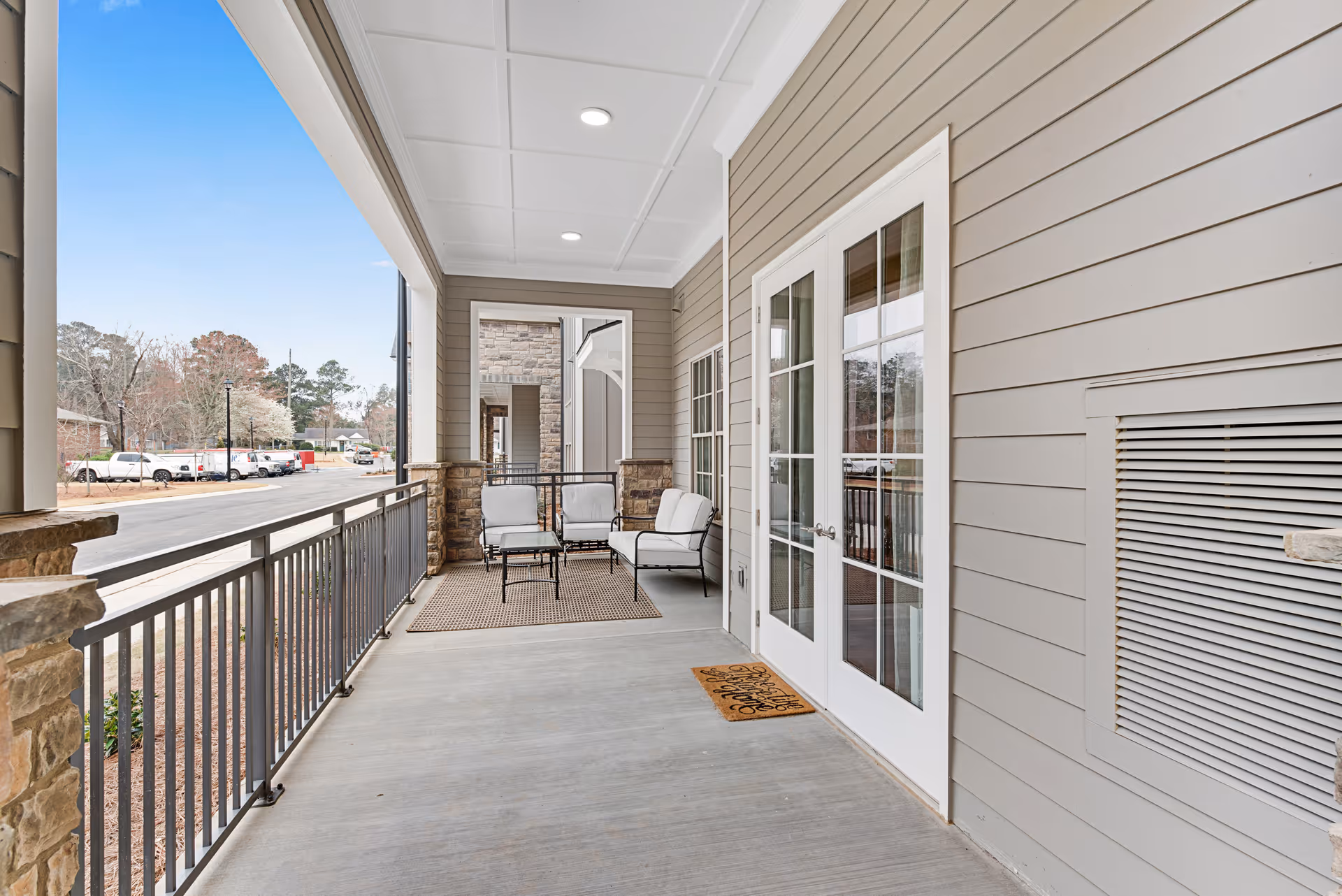 Covered exterior porch with seating and railing outside a senior living building overlooking the street.