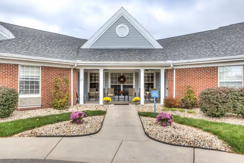 Brick single-story building front with a covered entrance, central walkway, and landscaped rock beds with potted flowers.