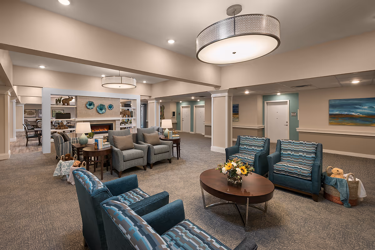 Spacious furnished common lounge with multiple seating groups, a coffee table with flowers, and a fireplace in the background.