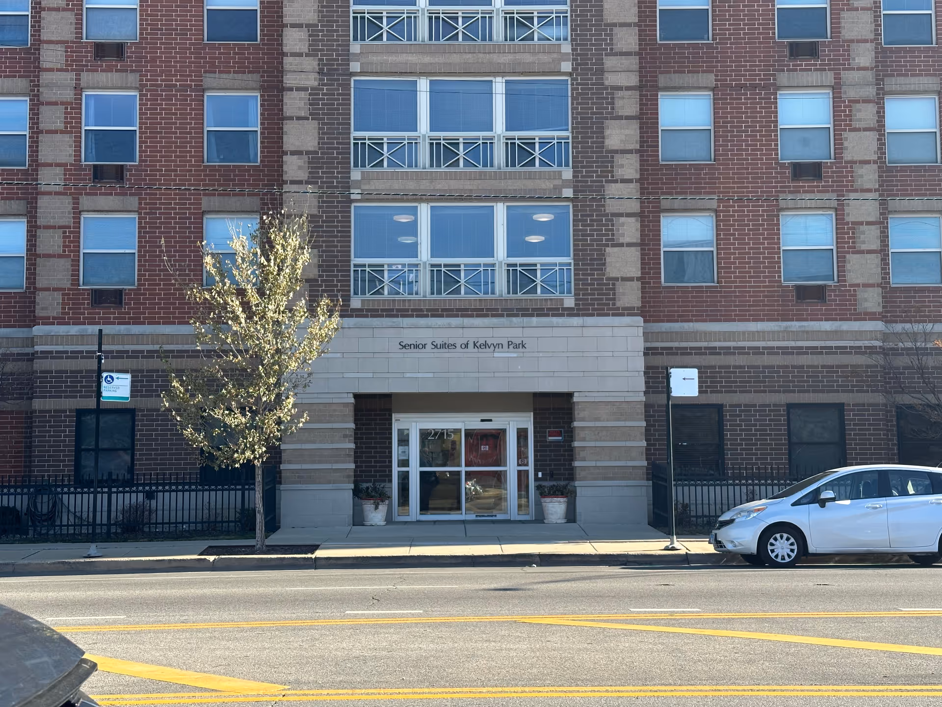 Brick facade and main entrance of the Senior Suites of Kelvyn Park building on a city street.
