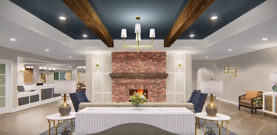 A spacious and well-lit living room area featuring a brick fireplace with a wooden mantel in the center. The ceiling has exposed wooden beams and a modern chandelier. There are two blue armchairs and a beige sofa facing the fireplace, with side tables and lamps on either side. The room has light-colored walls and wood flooring, with additional seating and decor visible in the background.