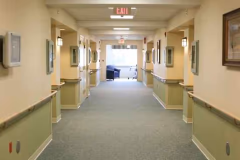 Long, well-lit corridor in a senior living facility with wall handrails and artwork.