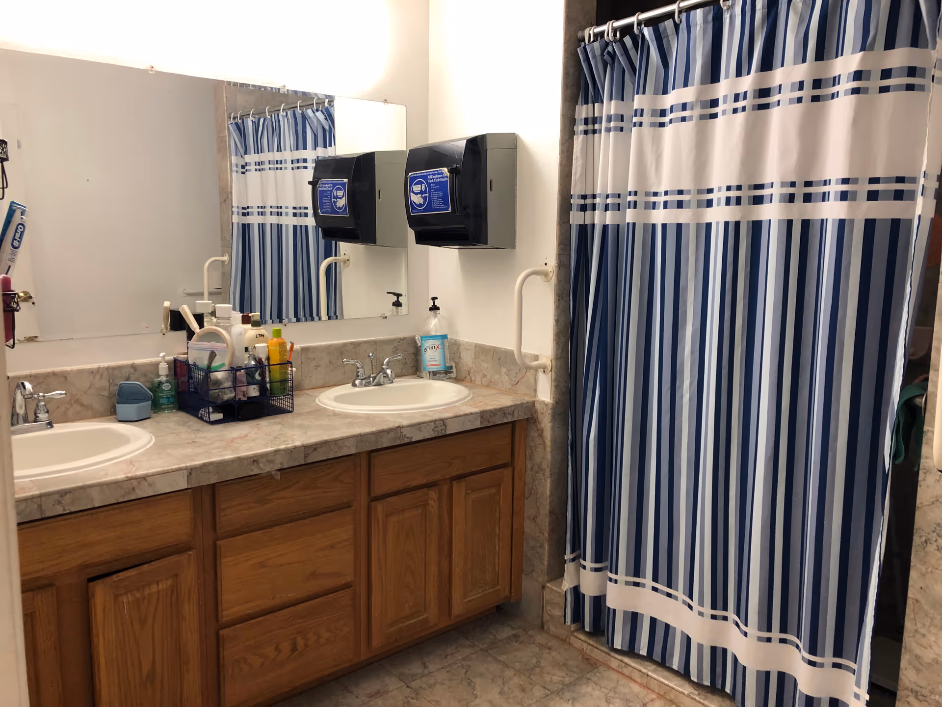Double-sink bathroom with striped shower curtain, mirrors, and wooden cabinets under a marble countertop.