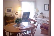 Round wooden dining table and chairs in a cozy living area with sofa, lamps, and plants.
