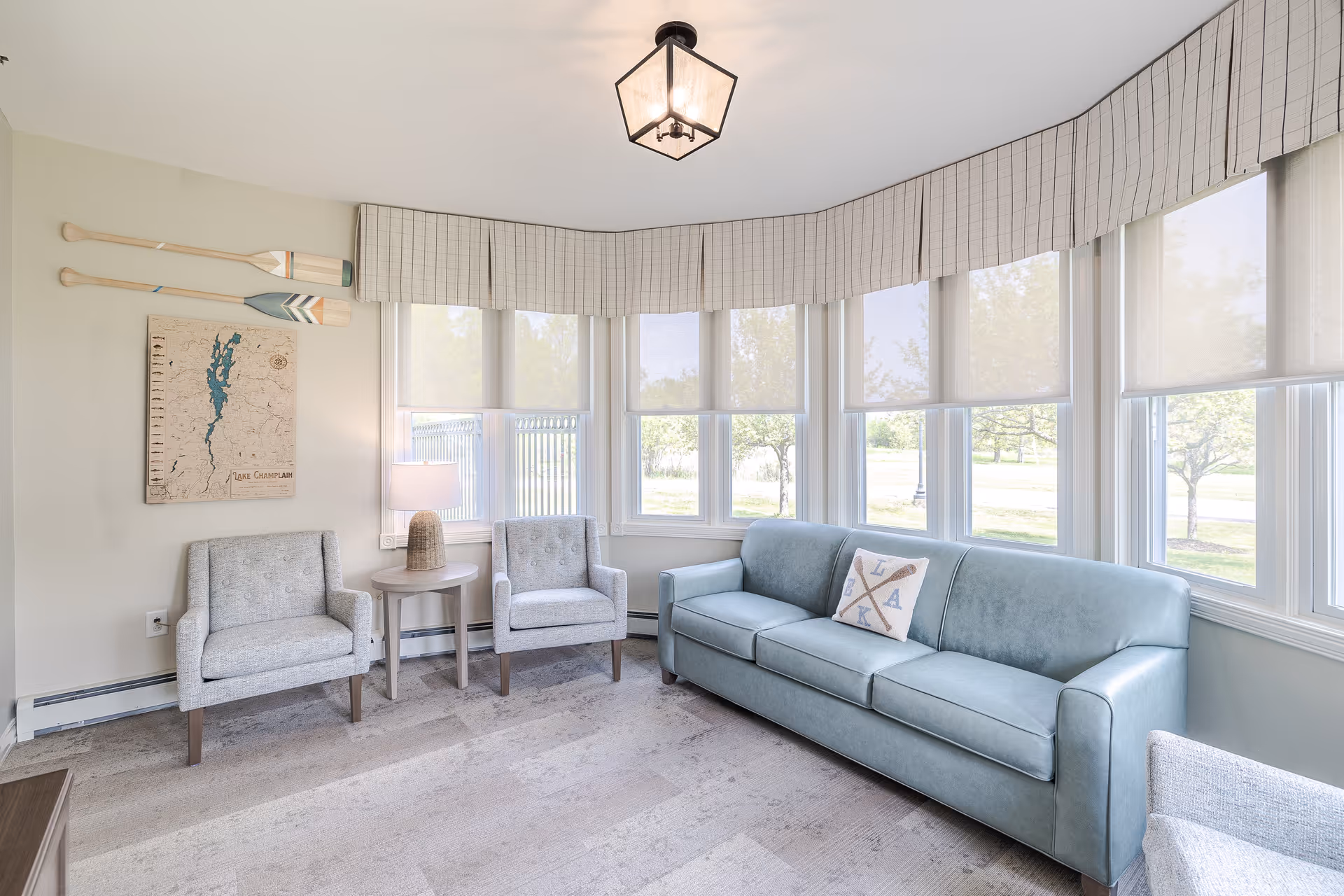 Bright living room lounge with a blue sofa, two pale chairs, and bay windows.