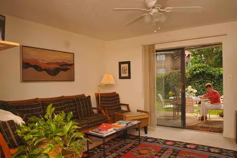 Cozy living room with plaid sofa, plants, coffee table, and sliding door to outdoor patio.