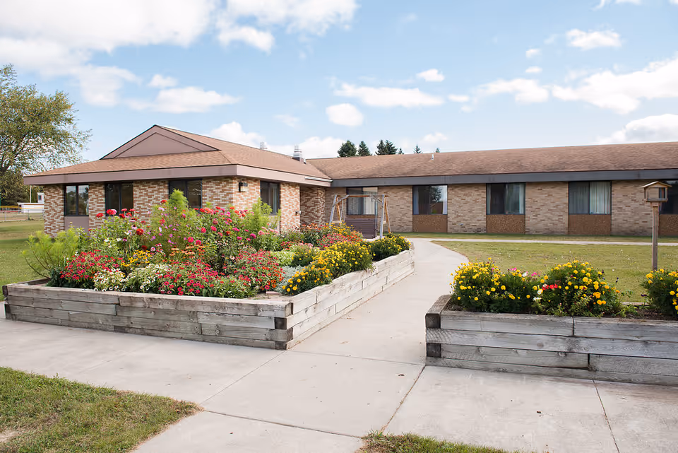 Single-story brick senior living building with raised wooden flower beds and a paved walkway leading to the entrance.
