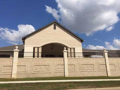 Front view of a beige brick senior care facility with a gated entrance.