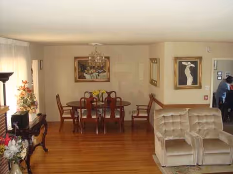 Sunlit senior living common area with a round dining table and beige seating.