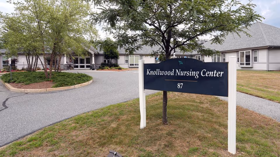 Front entrance of Knollwood Nursing Center with a black sign reading 'Knollwood Nursing Center' and a circular driveway in front of a single-story building.
