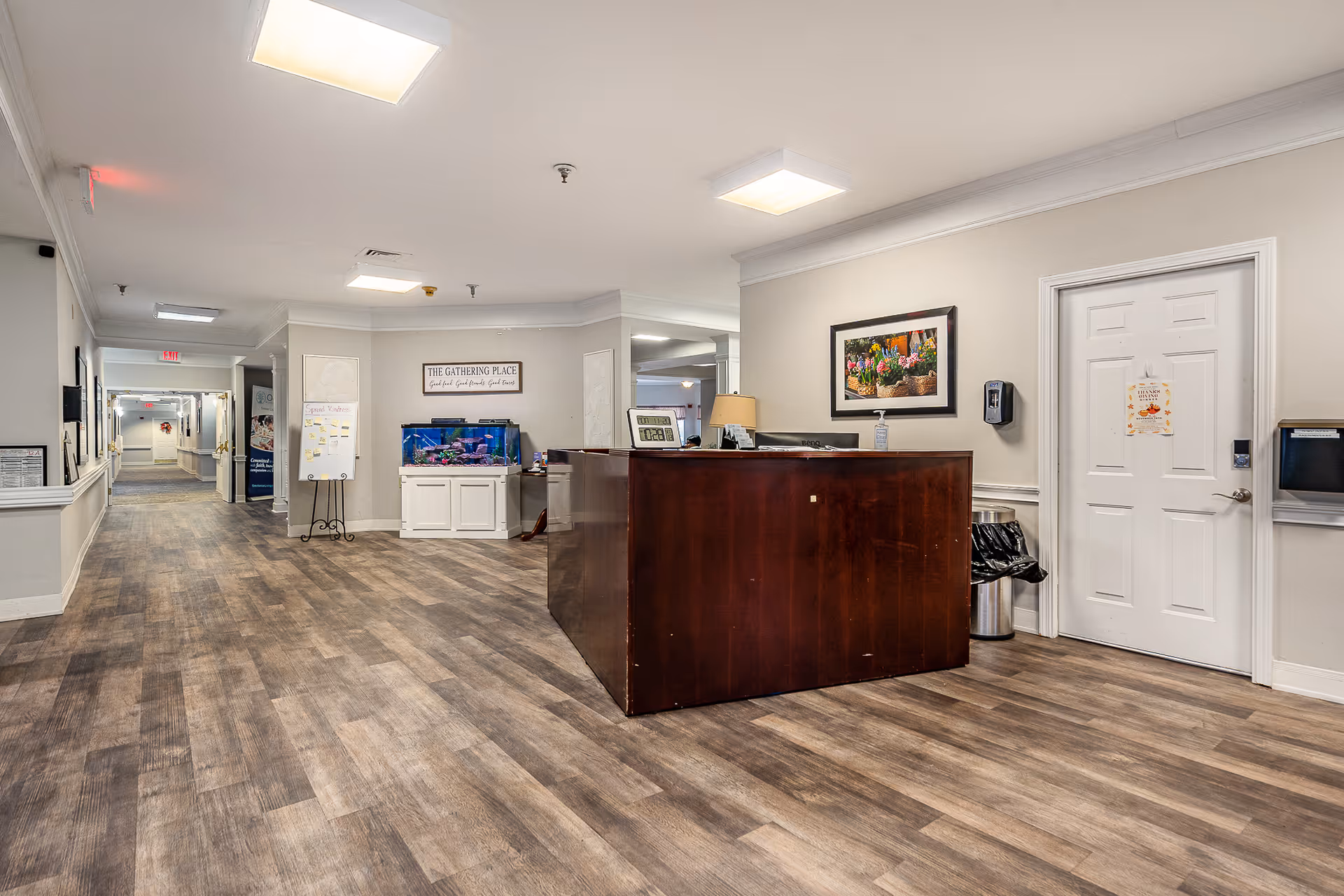 Reception desk and long hallway in a senior living facility lobby with an aquarium and framed artwork on the wall.
