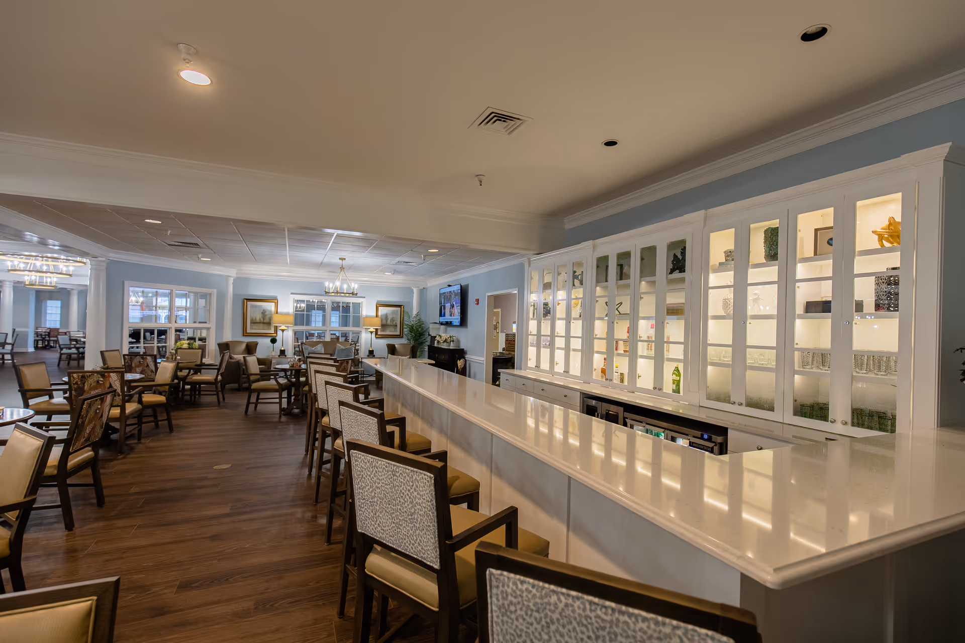 Spacious dining and lounge area with a long white bar, barstools, and multiple seating tables.