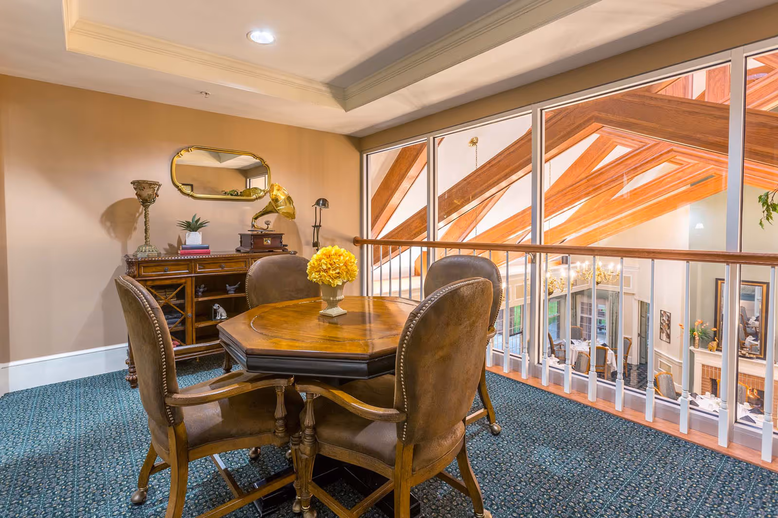 Small seating area with a wooden round table and four leather chairs beside a railing overlooking an atrium with exposed wooden beams.