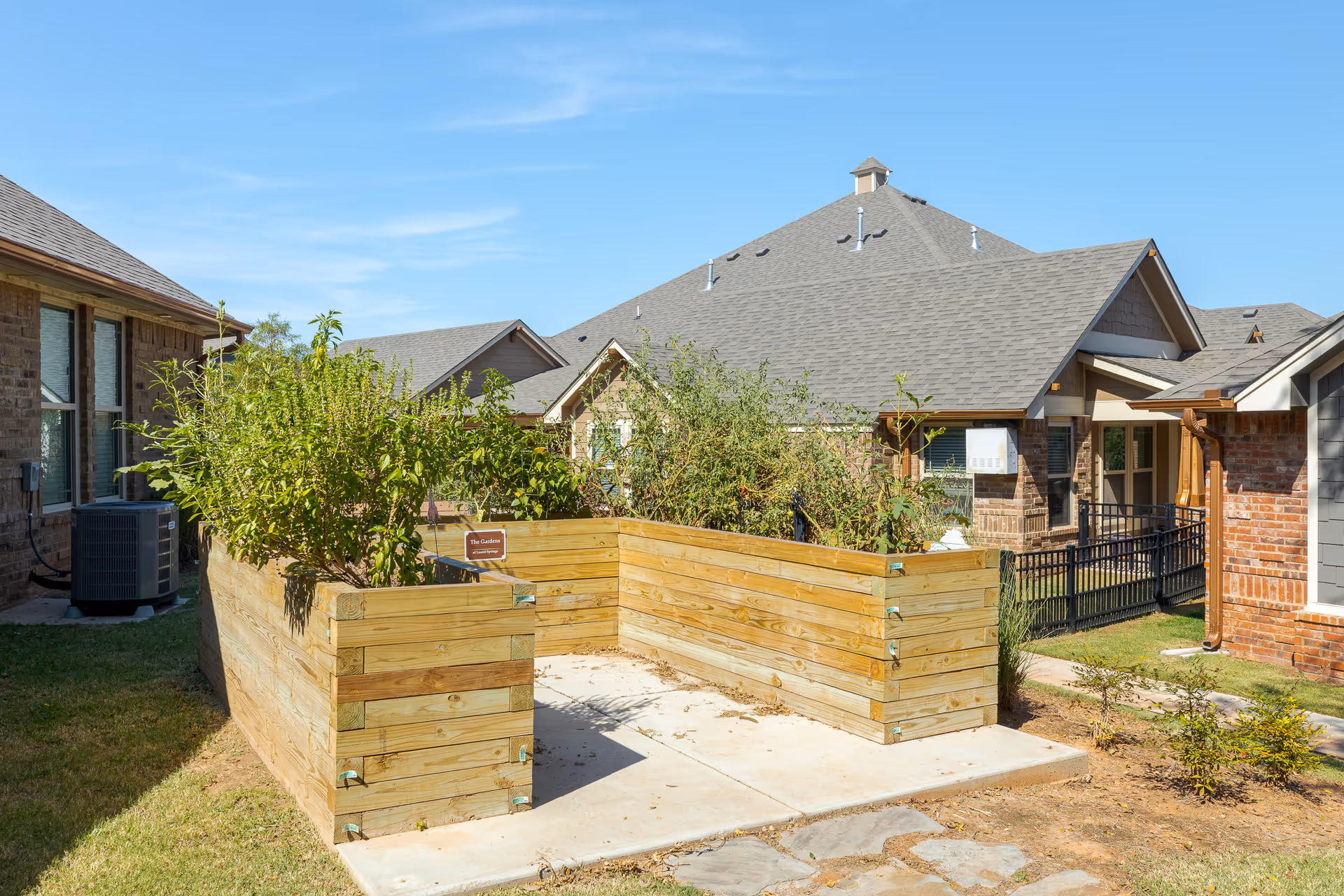 Raised wooden planter boxes filled with greenery in an outdoor courtyard in front of single-story residential buildings.