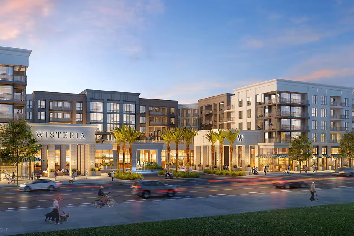 Exterior view of Wisteria at Warner Center, a modern multi-story senior living facility with large windows, balconies, palm trees, and people walking and biking along the street in front during dusk.