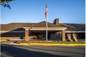 Exterior view of a single-story brick building with a covered entrance and an American flag on a flagpole in front, under a clear blue sky.