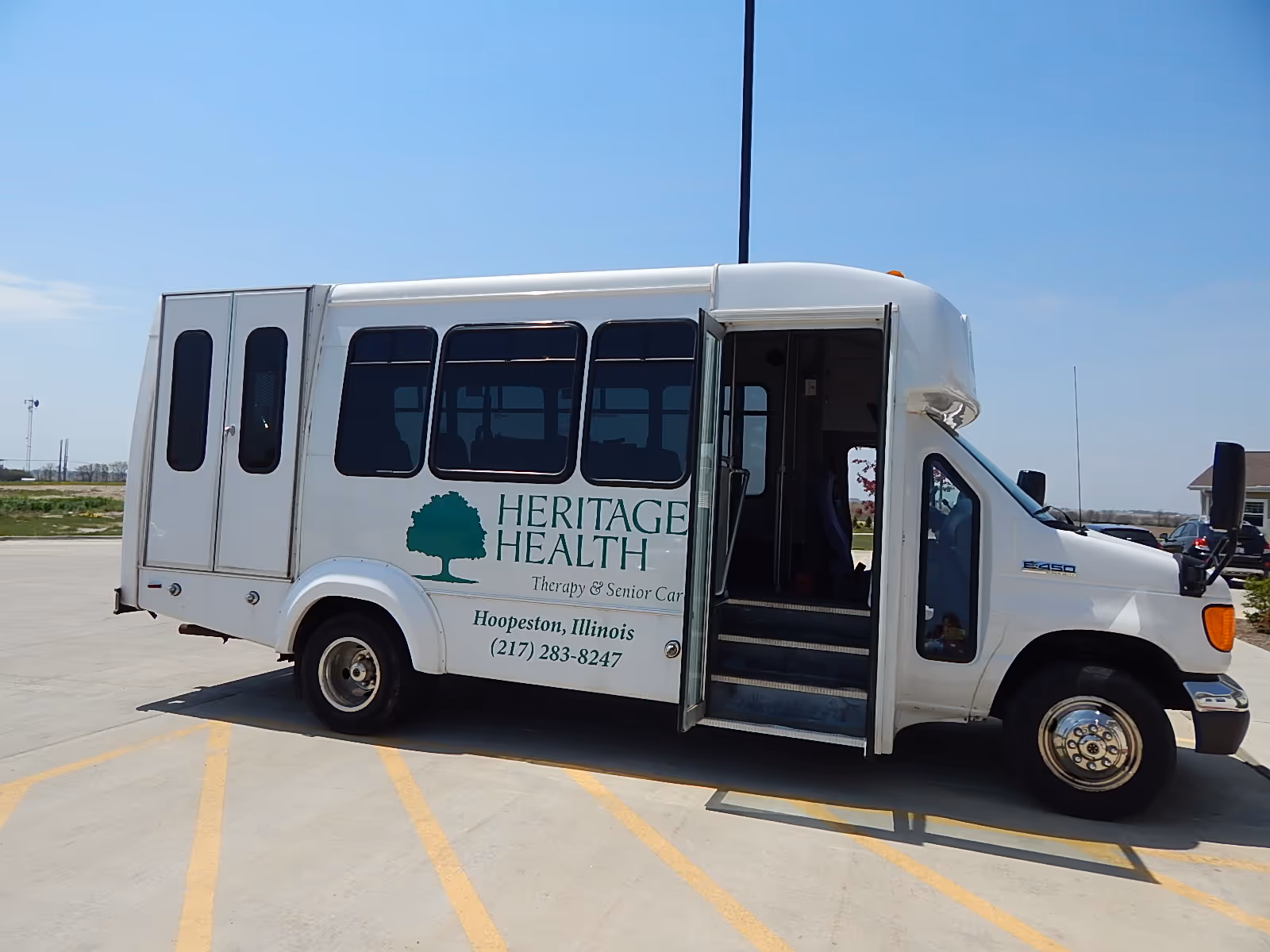 A side view of a white bus labeled 'Heritage Health: Therapy & Senior Care' parked in a lot.