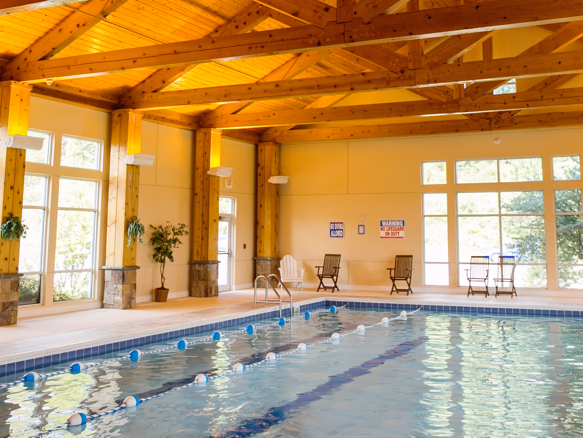 Indoor lap pool with lane markers in a wood-beamed room with chairs and large windows along the side.