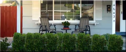 Front porch of a home with two chairs, a small table, and a potted plant.