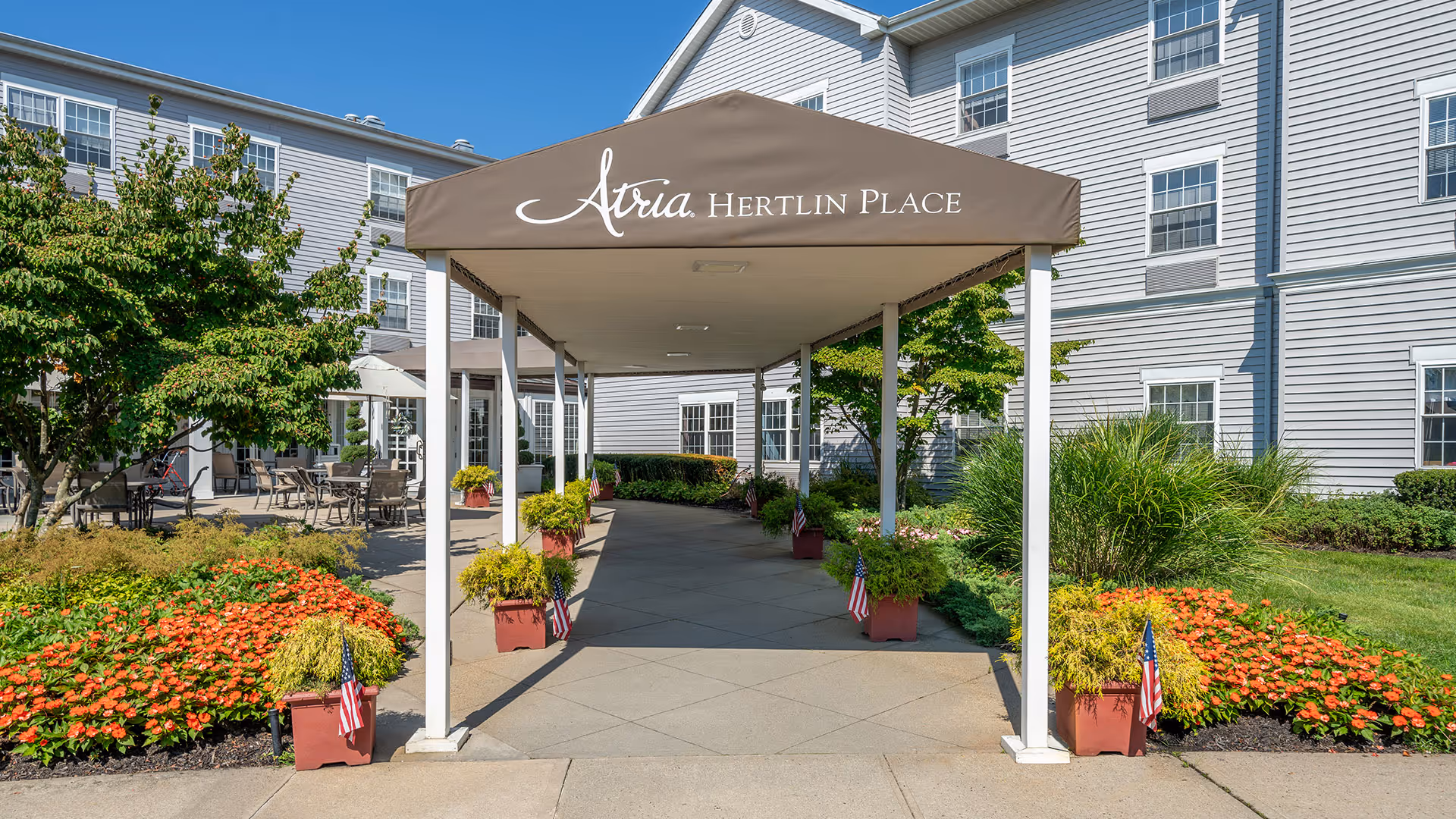 Covered entrance canopy labeled "Atria Hertlin Place" leading to a landscaped walkway and the building facade.