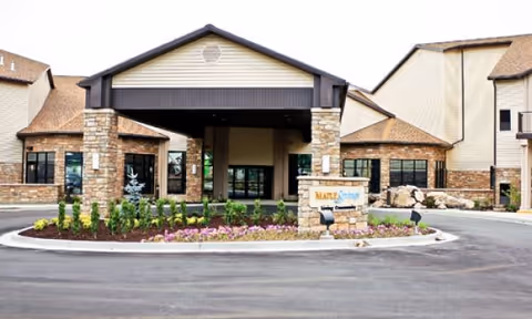 Front exterior view of Maple Springs of Brigham City facility showing a covered entrance with stone pillars, landscaped flower beds, and a sign with the facility name.