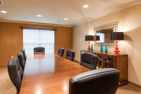 A long wooden conference table with black leather chairs in a well-lit dining room.